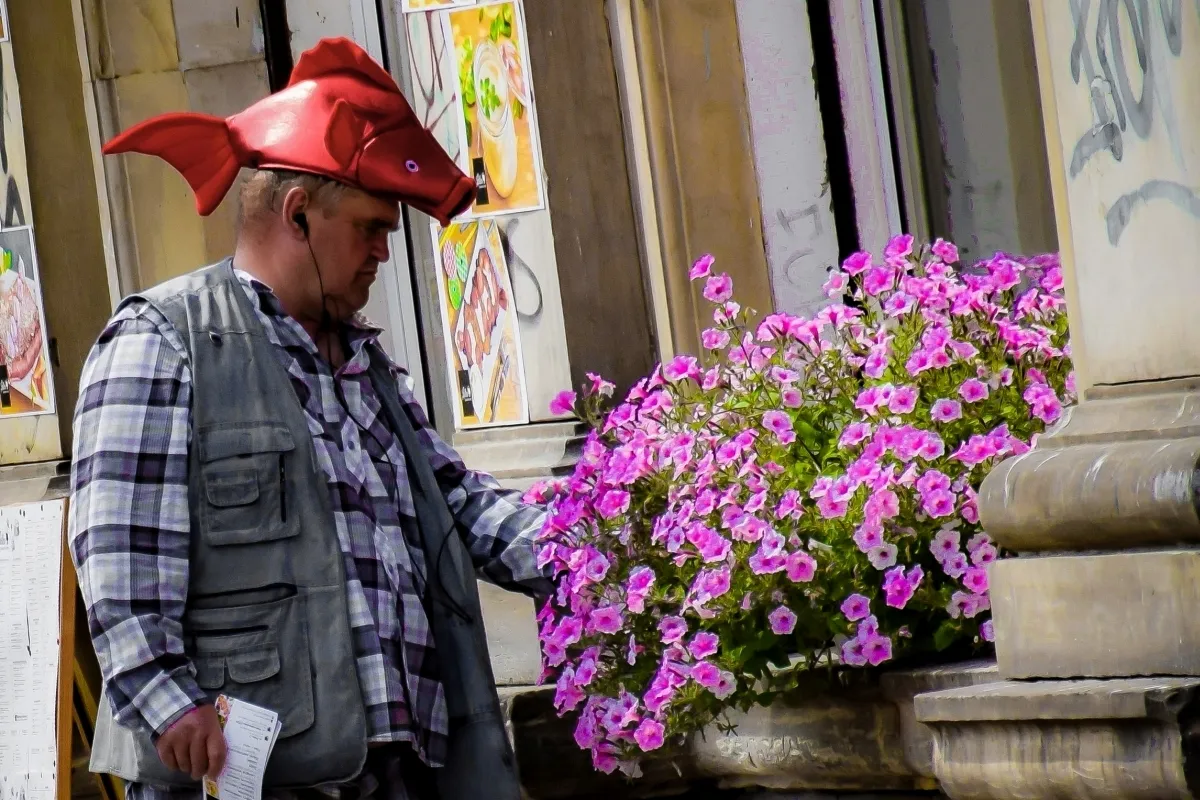 Man wearing a red fish hat beside pink flowers